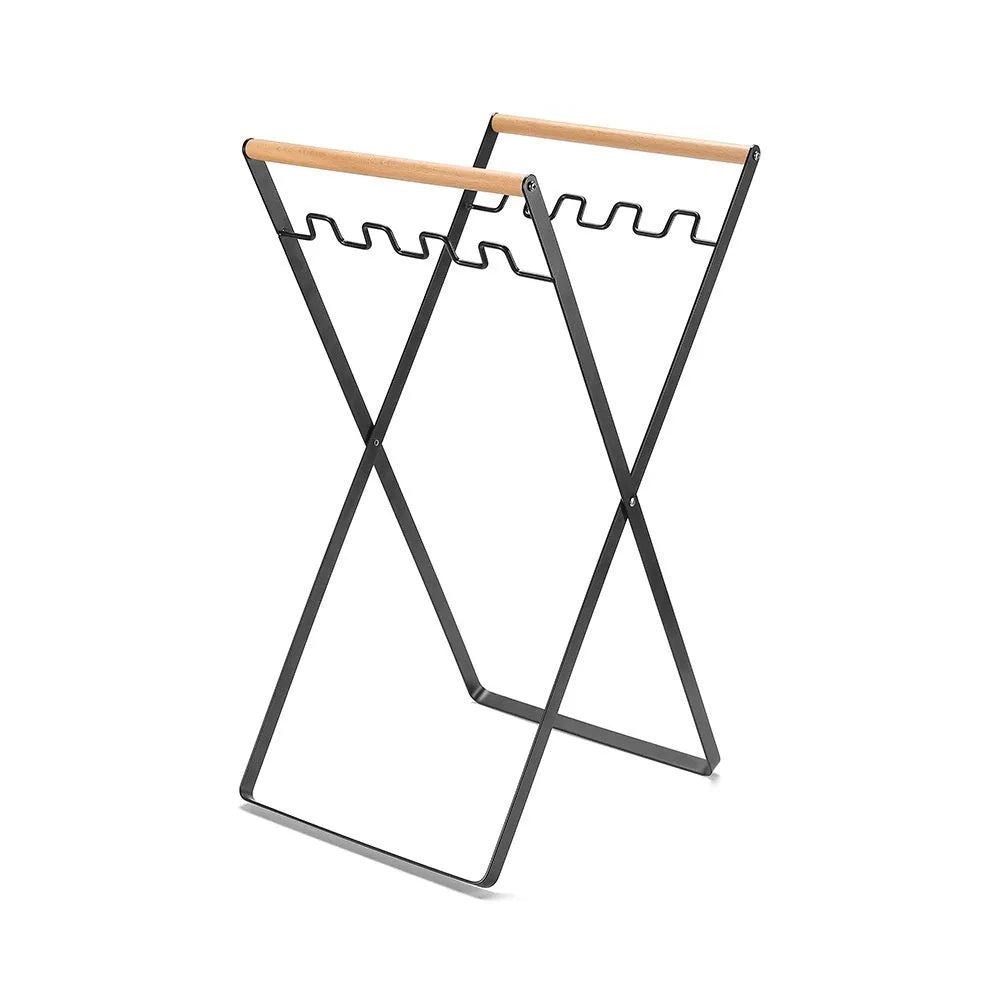 Black folding iron trash rack with wooden handle holding a bin bag outdoors.