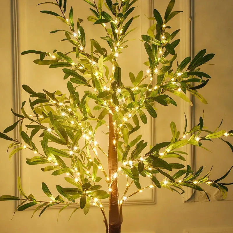 Tall artificial olive tree lamp with warm white LED lights illuminated in an outdoor courtyard setting.