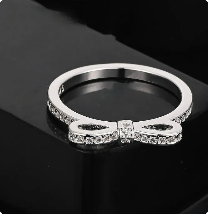Silver couple's ring with a bow shape and sparkling zircon crystal rhinestones on a finger.