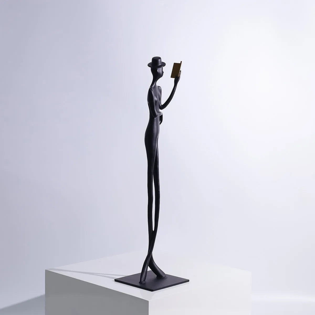 Black aluminium desktop sculpture of a woman reading, measuring 12cm wide by 51cm tall.