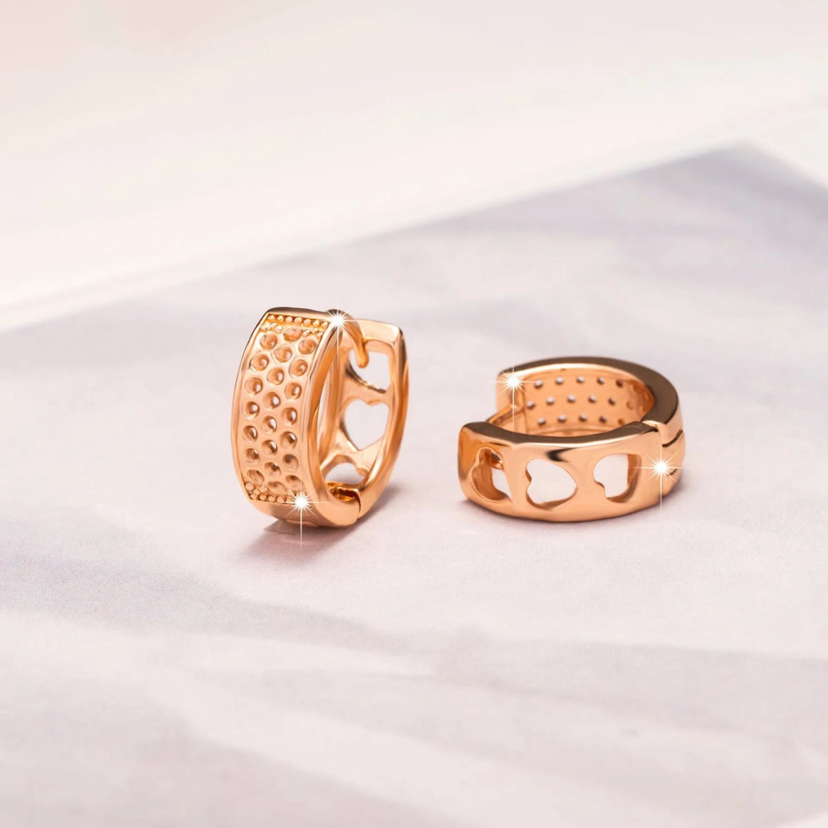Rose gold electroplated drop earrings with three hollowed-out hearts in a circular arrangement.