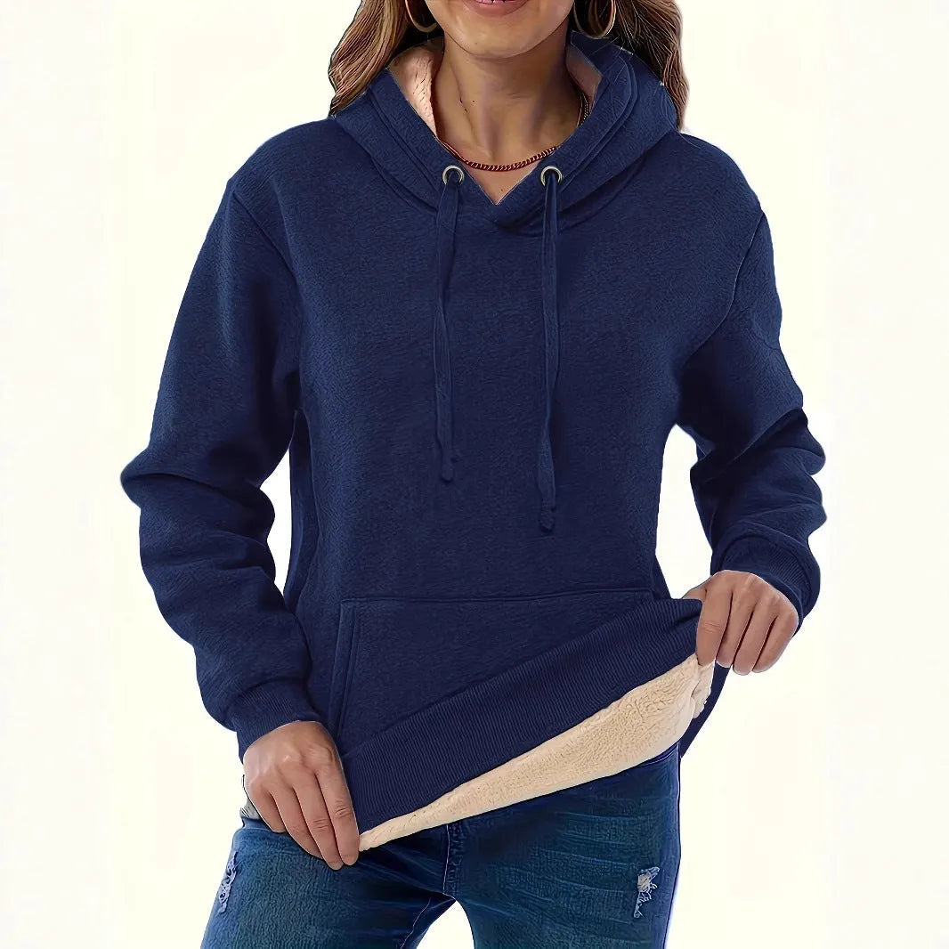 Woman wearing a loose grey hooded sweater with a front kangaroo pocket.