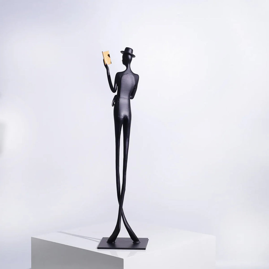 Black aluminium desktop sculpture of a woman reading, measuring 12cm wide by 51cm tall.