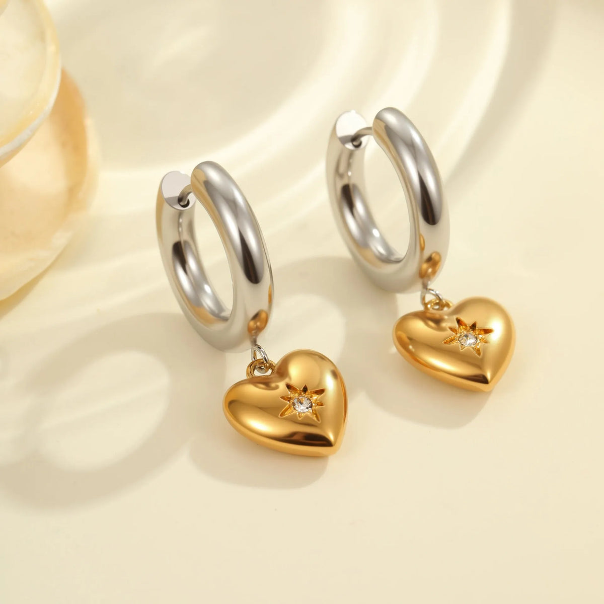 A pair of gold-coloured stainless steel earrings featuring a Christmas tree design and a heart shape with star details.