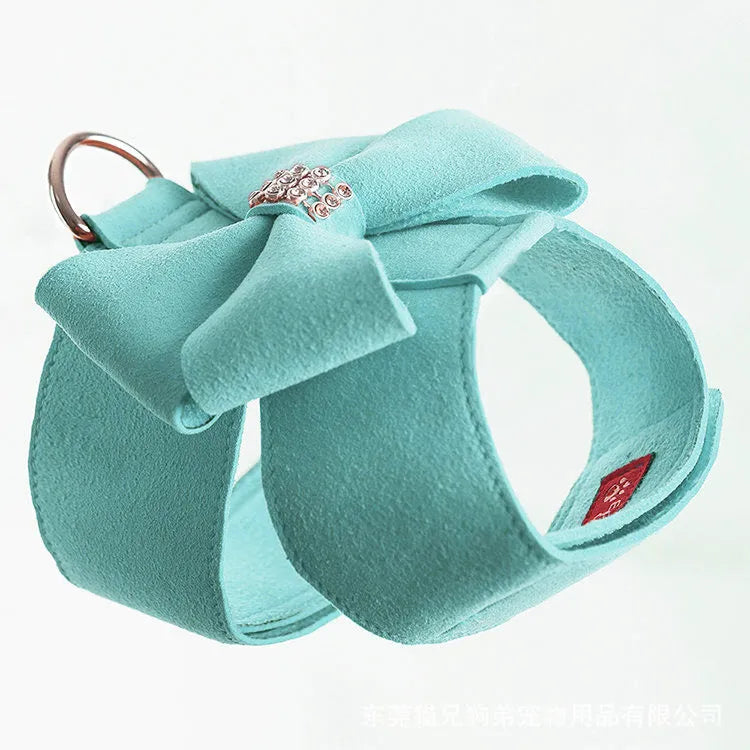 A pink microfiber puppy chest strap harness with a large central bowknot, showing adjustable buckles.