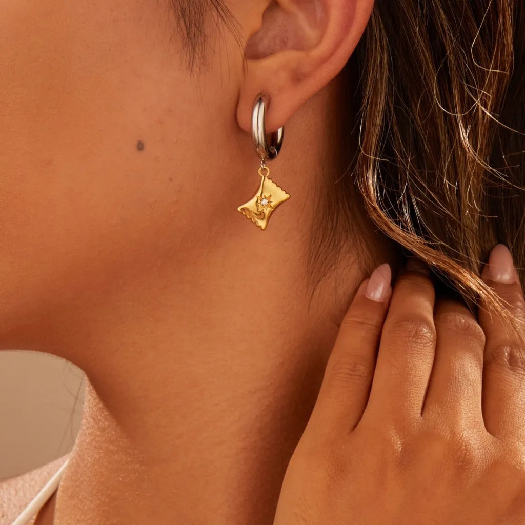 A pair of gold-coloured stainless steel earrings featuring a Christmas tree design and a heart shape with star details.