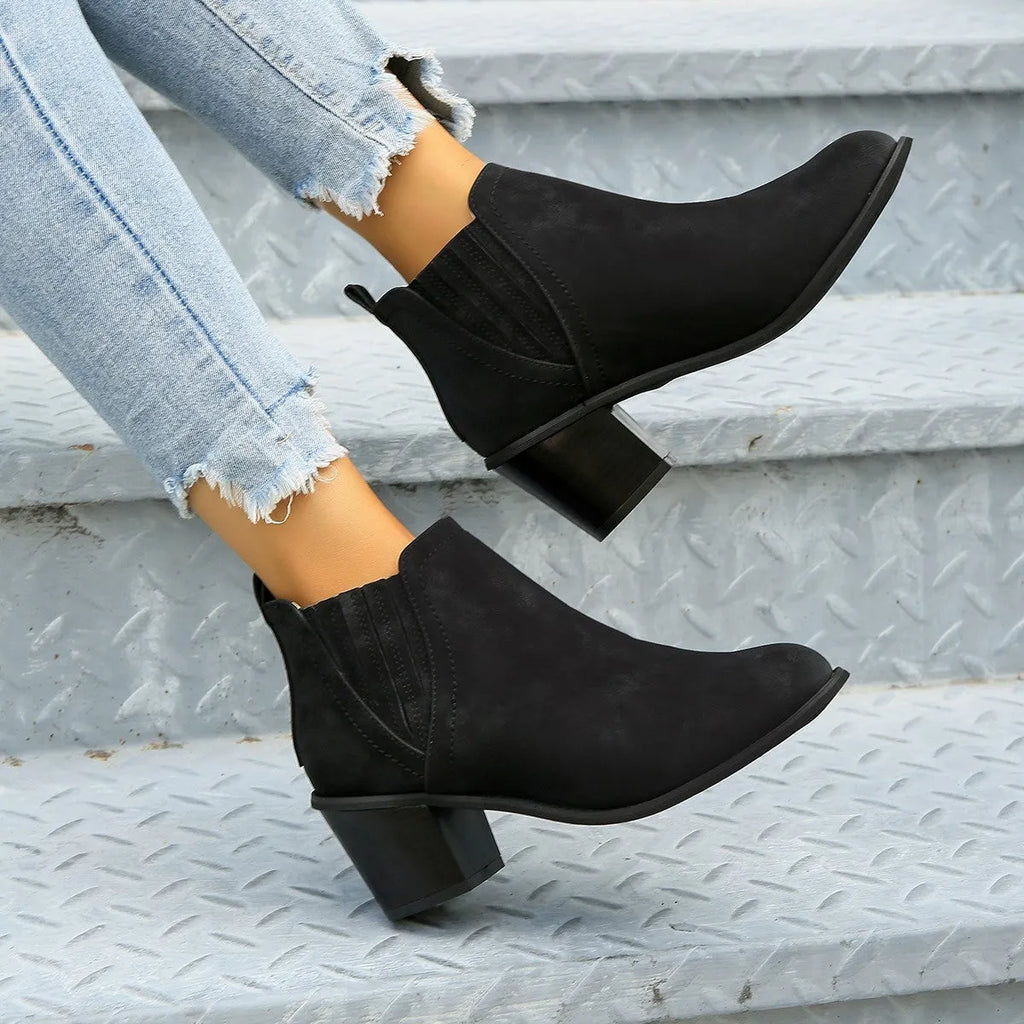 Women's black ankle boots with pointed toes and thick square heels on a solid background
