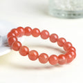 Loose polished cherry red agate beads in various sizes for bracelet making on a white surface.