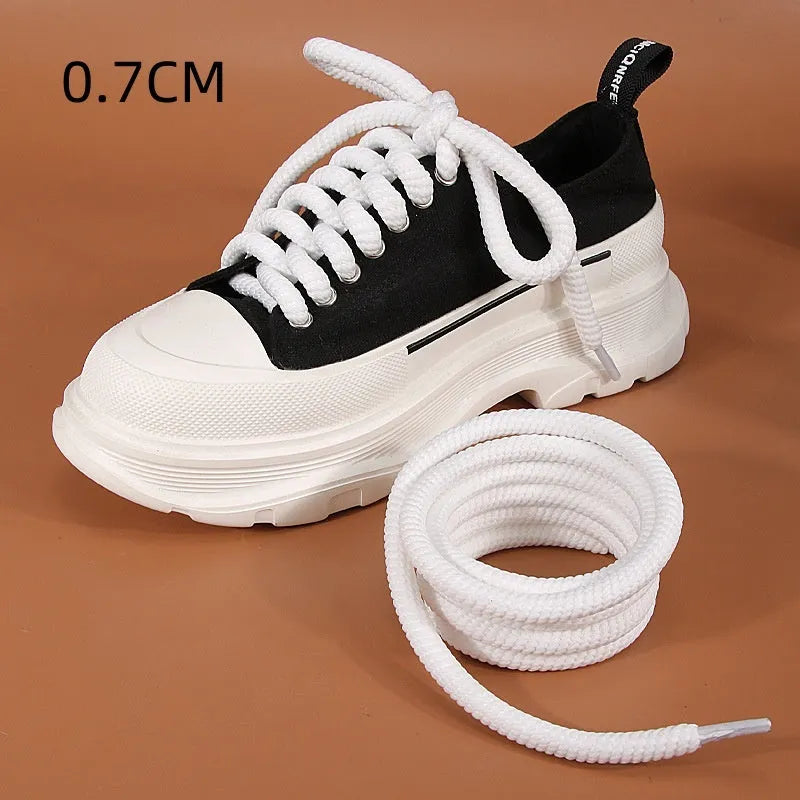 Round white woven shoelace with 10mm diameter next to a beige and black lace on a grey background.